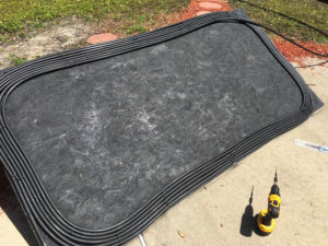 Close-up of drilled holes and zip ties securing hose to plywood